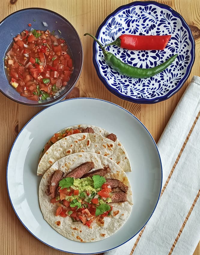 un plato con dos tacos de carne, guacamole y pico de gallo